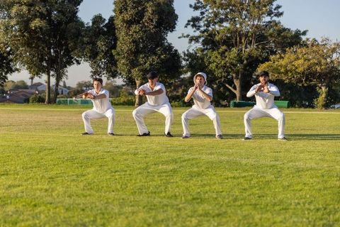 Four cricket players practicing catching drill on club field in white kit and caps