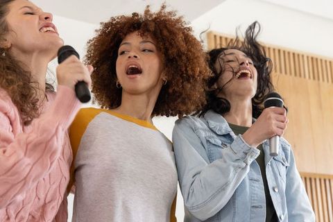 Multiracial female friends singing energetically holding microphones in rehearsal room