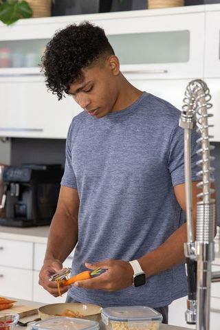African american man peeling carrots at modern minimalist kitchen counter with smartwatch