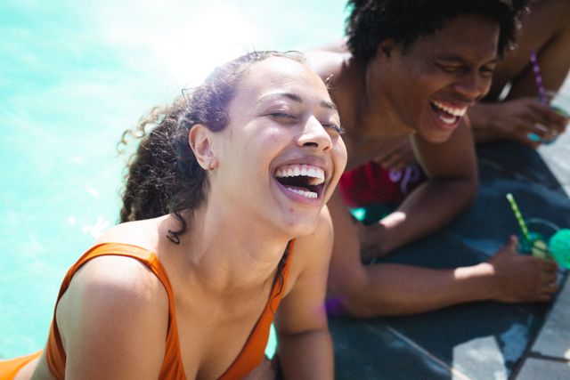 Portrait of cheerful multiracial woman enjoying drinks with friends at poolside on sunny day. unaltered, people, enjoyment, lifestyle and alcohol concept.