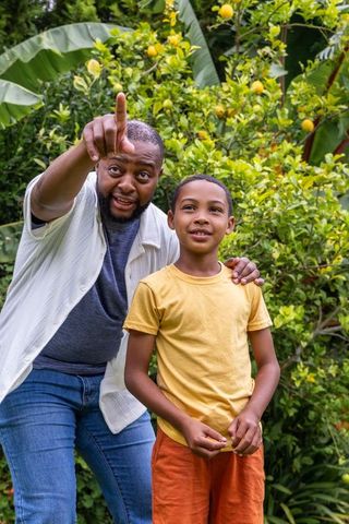 Black father pointing and guiding son in backyard lemon tree garden mentoring moment