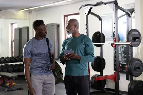 African american personal trainer coaching young male client in modern gym weight room