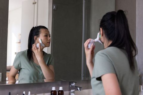 African american woman using electric facial massager at mirror for daily skincare routine