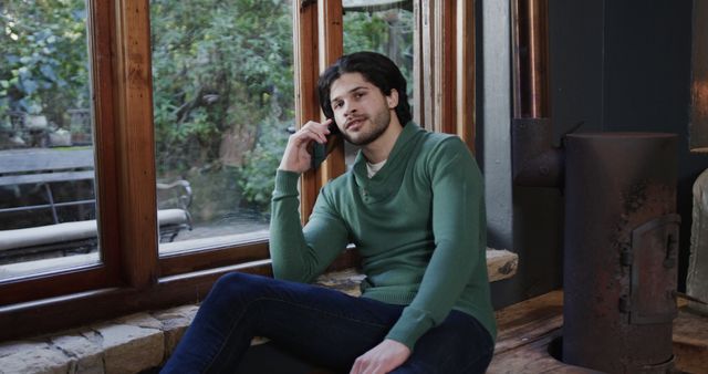 Young man talking on smartphone while sitting by window - Download Free Stock Images Pikwizard.com