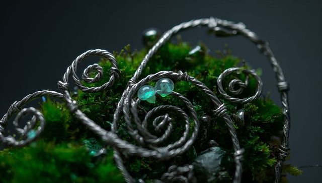 Wire-wrapped spiral jewelry resting on vibrant green moss with teal glass beads