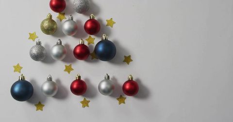 Arranging festive baubles into christmas tree shape on white backdrop with gold stars