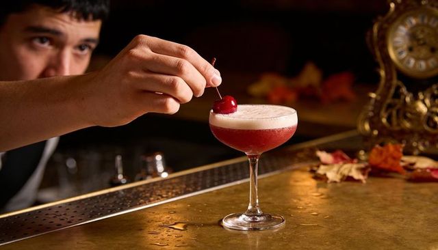 Bartender garnishing frothy cranberry cocktail with cherry on vintage bar, autumn mood