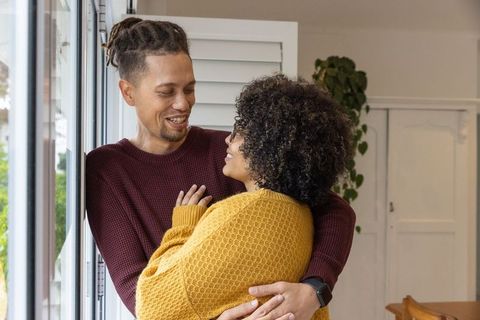 Couple embracing by window wearing mustard and burgundy knit sweaters, cozy home intimacy