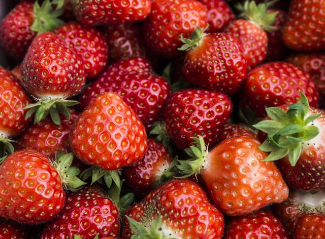 Close-up view of a pile of fresh strawberries with vibrant red color and green stems. Ideal for use in food blogs, healthy eating campaigns, nutritional articles, kitchen posters, or any marketing materials related to fresh fruits, farming, and organic produce.