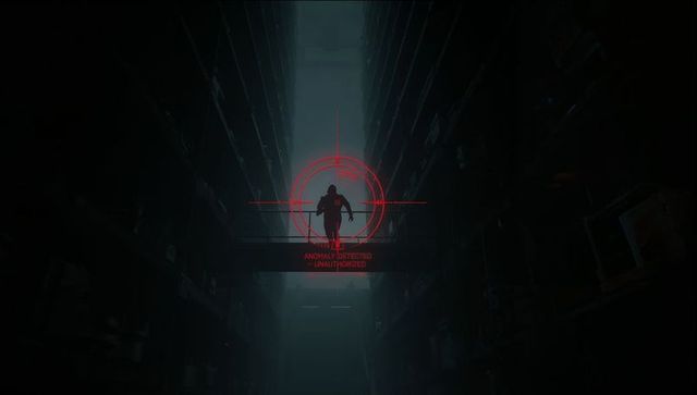 Hooded figure walking on elevated catwalk framed by red targeting reticle in dark warehouse