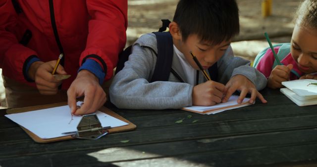 A diverse group of children are focused on drawing or writing activities outdoors, with copy space - Download Free Stock Photos Pikwizard.com