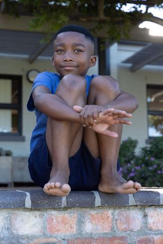 African american boy sitting on brick porch wall hugging knees smiling in shaded yard