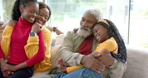 Multigenerational Black family cuddling and laughing on bright cozy living room couch