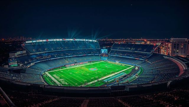 Floodlit nfl stadium at night over urban skyline featuring empty seats and bright turf