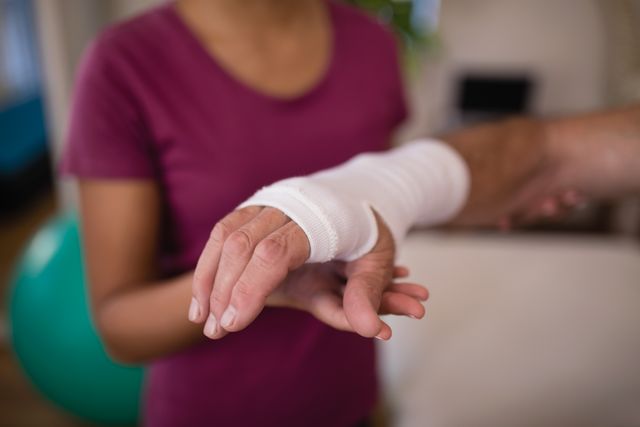 Close-up of senior male patient with bandage on wrist by female therapist at hospital ward