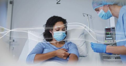 Nurse preparing injection while patient rolling up sleeve at hospital bedside wearing mask