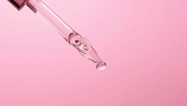 Glass dropper pipette creating droplet on pink background