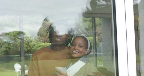 African American couple embracing by window holding mug cozy garden morning romance