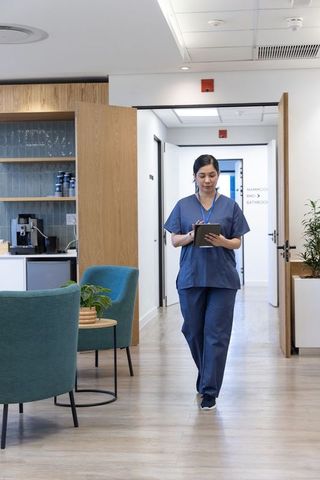 Female nurse walking clinic corridor consulting tablet in modern healthcare facility