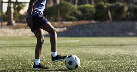 African american teen pausing with soccer ball on synthetic turf practicing ball control