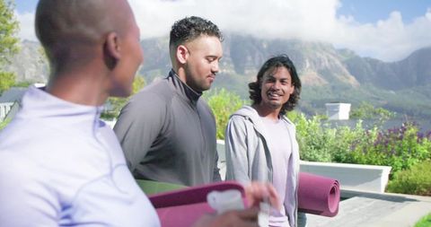 African american friends walking with yoga mats on waterside terrace, smiling