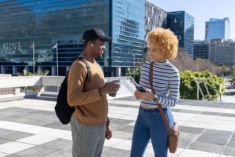 African american friends chatting and sharing smartphone on sunny modern urban plaza