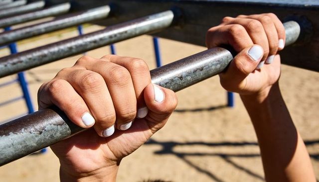 Woman's hands gripping metal playground bar with white nail polish and sunlit shadows