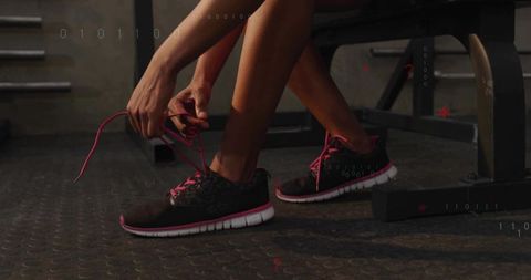 Woman tying pink-laced running shoes on gym bench preparing for strength training