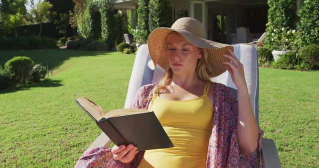 Caucasian woman reading a book while sunbathing on a deck chair in the garden. summer holiday and leisure concept.
