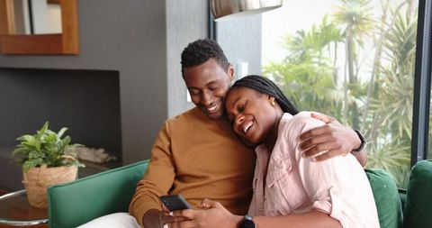 Joyful Couple Relaxing on Couch with Smartphone