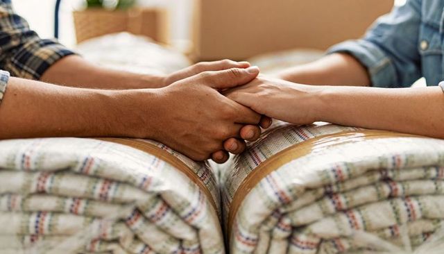 Couple holding hands over packed comforters conveying support and warmth during move