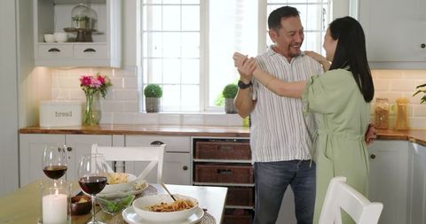 Couple Dancing in Sunlit Kitchen After Homemade Dinner with Wine and Candlelight