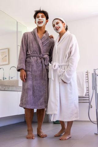 Asian man and african american woman enjoying spa morning wearing robes and face masks