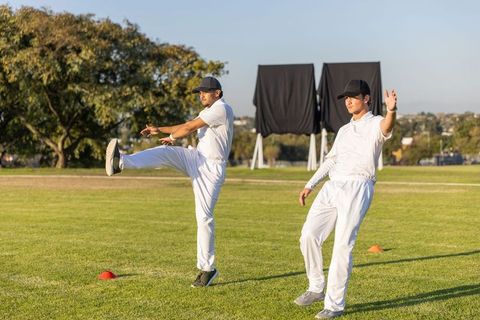 Cricket teammates warming up on grassy pitch with sight screens and orange cones