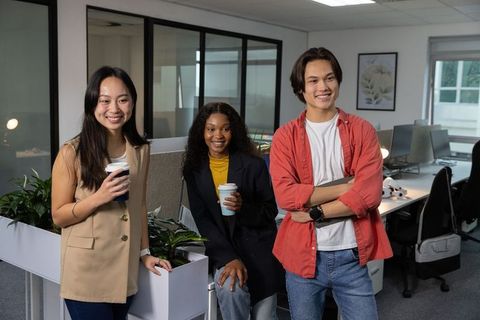 Smiling diverse coworkers enjoying coffee break in modern open-plan office with greenery
