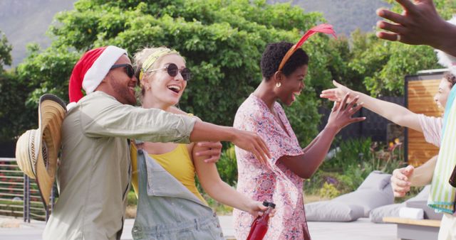 Group of friends dancing and laughing at an outdoor party. One wearing a Santa hat, another with a headband, all having fun and expressing joy. Perfect for themes related to social events, celebrations, joy, and summer fun.