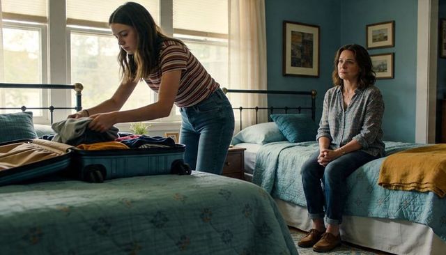 Teen daughter packing suitcase while worried mother watching on beds in cozy bedroom