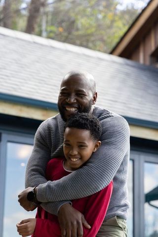 African american father hugging smiling preteen son on home porch showing wristwatch