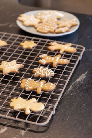 Gingerbread cookies cooling on wire rack with white icing on dark stone countertop