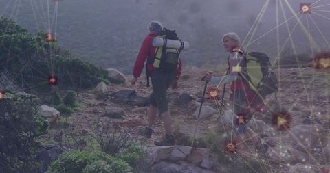 Middle-aged hikers trekking rocky ridge with backpacks and poles