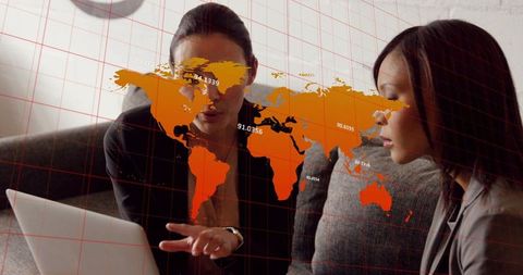 Women collaborating on laptop reviewing global analytics with orange world map overlay