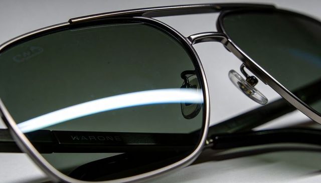 Aviator sunglasses capturing curved reflection on green lenses with visible metal logo
