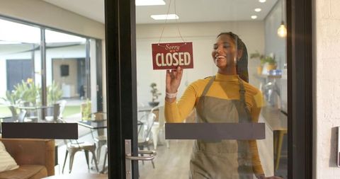 African american barista hanging closed sign on glass cafe door, modern coffeehouse closing