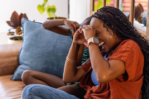 Laughing mother and daughter smiling and making heart hands on couch in cozy living room