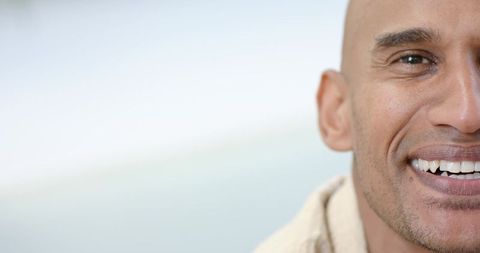 Smiling bald man with warm grin and stubble closeup against soft neutral bokeh background