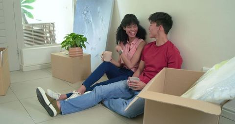 Unpacking and enjoying coffee in new home, african american woman and asian man laughing
