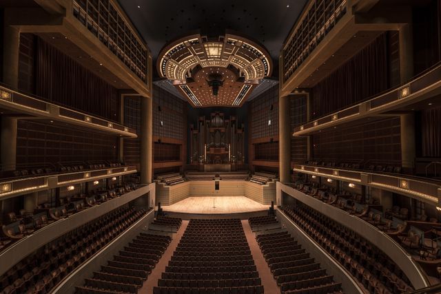 View of a magnificent, grand auditorium with a large stage and rows of empty seats. The interior architecture features luxurious materials and a sophisticated design. This setting is ideal for concerts, theatrical performances, or cultural events. Suitable for promotional material for event spaces, programs, or advertisements catering to music and performing arts communities.