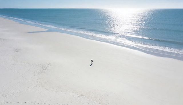 Solitary figure walking on vast white sand beach with turquoise sea and sparkling sunlight