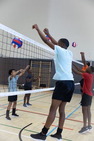 Male players jumping and blocking at volleyball net in indoor gym