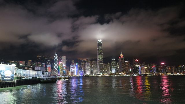 Hong Kong's skyline at night features brightly lit skyscrapers reflecting on calm harbor waters. Ideal for urban scenes, modern lifestyle depictions, and travel-related content emphasizing nightlife and city vibrance.